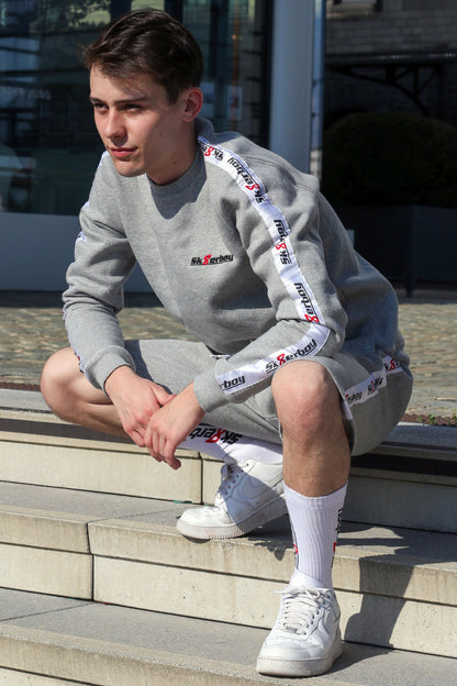 junger typ trägt grauen sk8erboy trainingsanzug in lang mit passender hose und sweatshirt zu seinen weißen nike sneaks sitzend mit crew socks